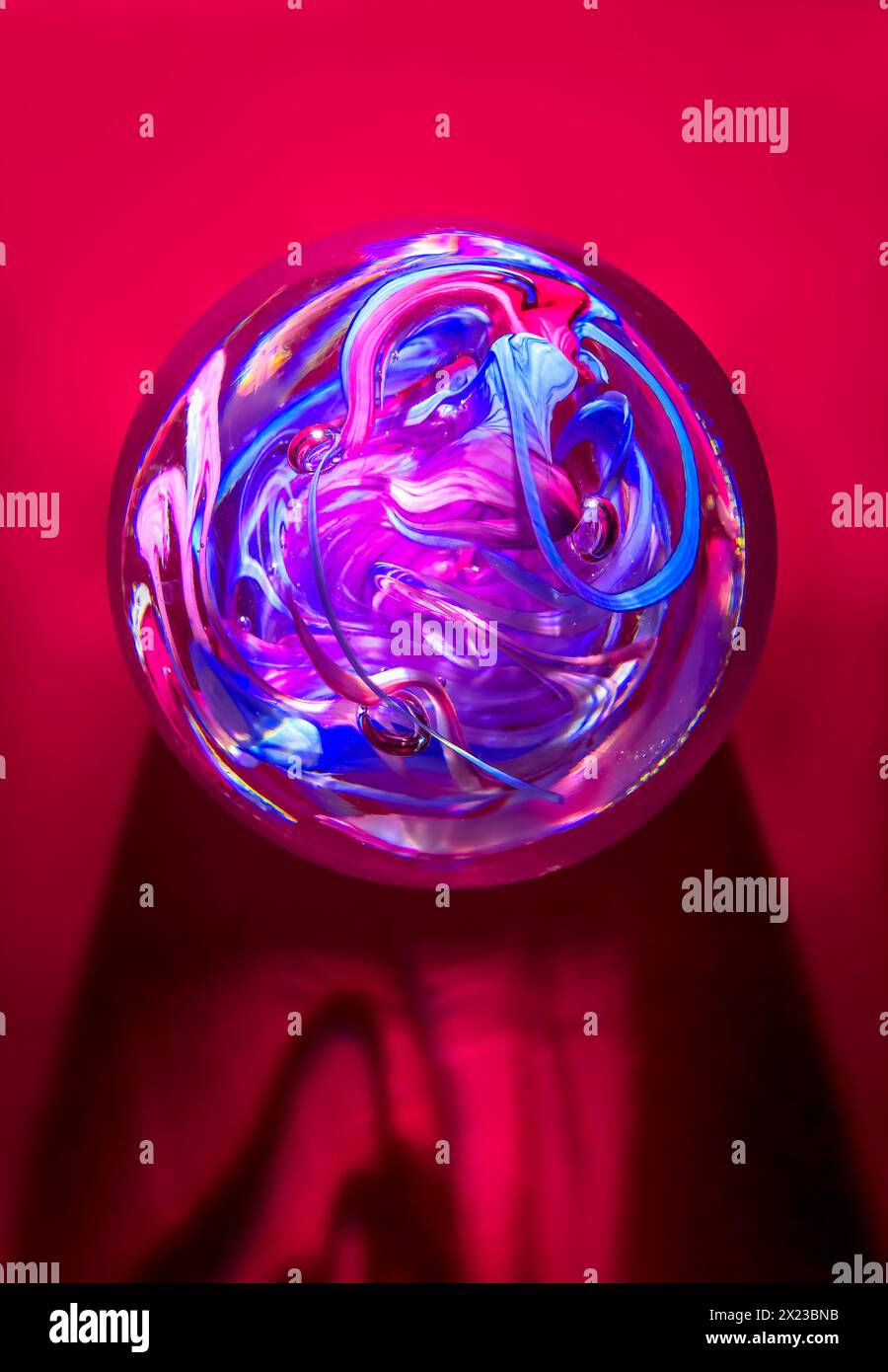 Colourful Glass Crystal Paperweight on a red background, with swirl pattern in a round ball shape. Concept of crystal Ball and fortune telling Stock Photo