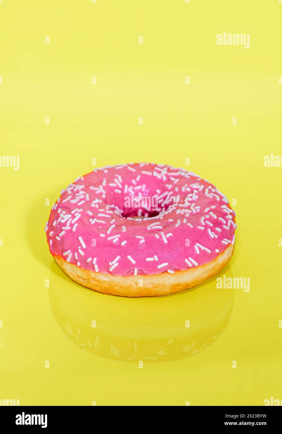 Pink iced Ring Doughnut on light yellow or lemon coloured background with sprinkles on Stock Photo