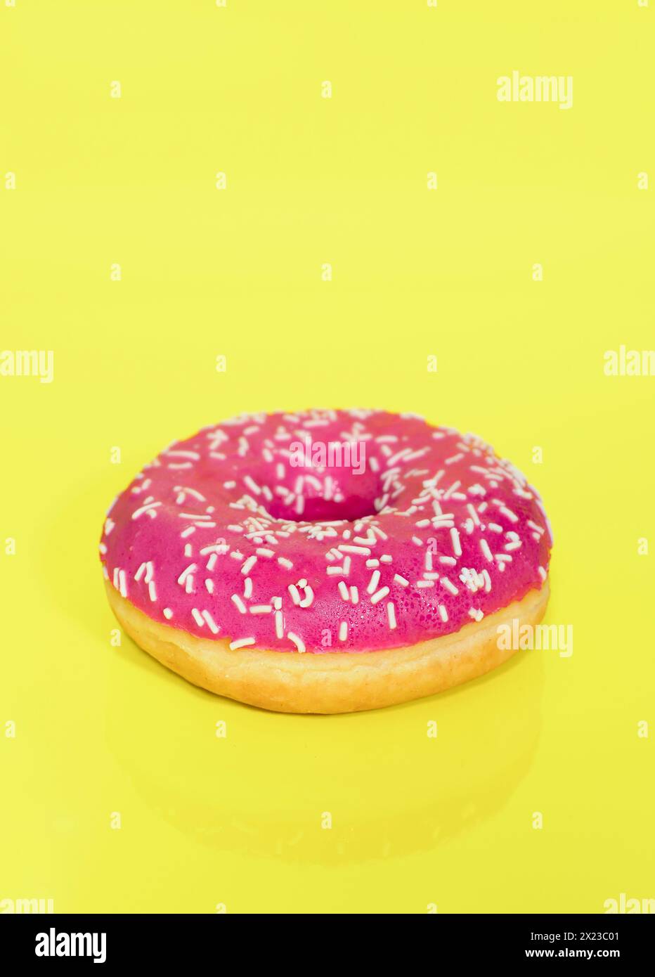 Pink iced Ring Doughnut with sprinkles on, taken on a yellow coloured background Stock Photo