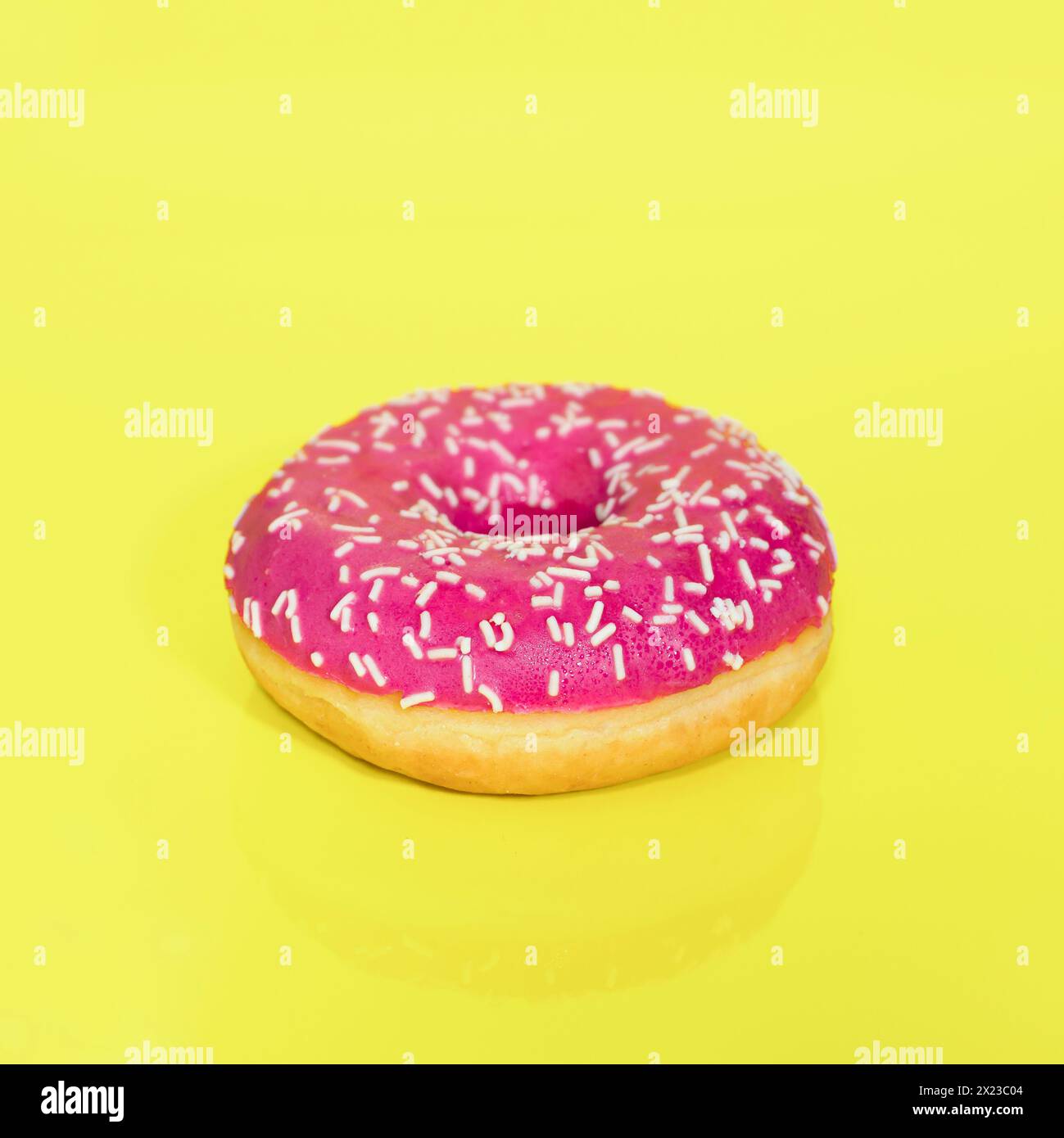 Pink iced Ring Doughnut with sprinkles on, taken on a yellow coloured