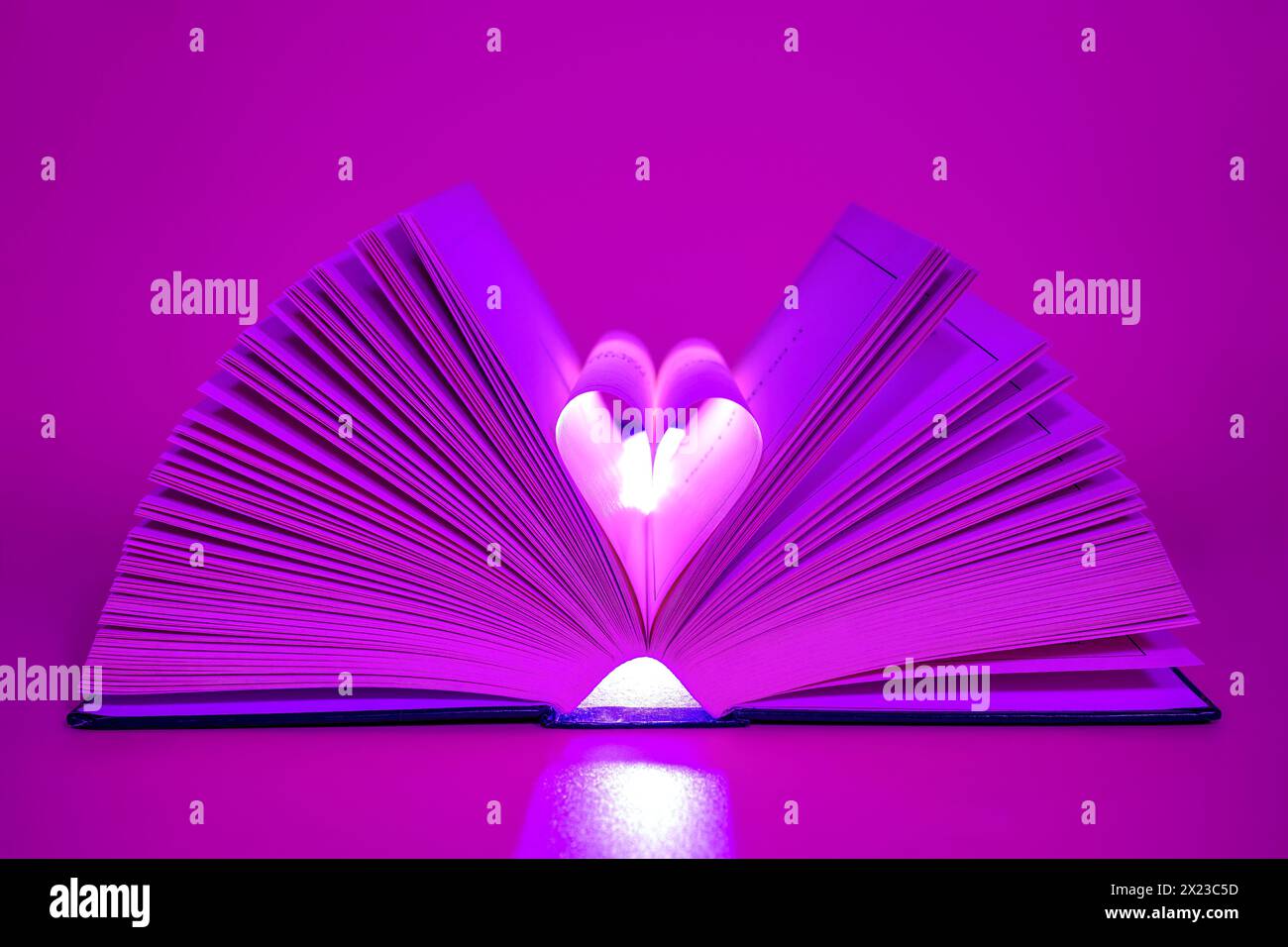 Open Book on pink/purple coloured background with middle pages turned into a heart shape Stock Photo