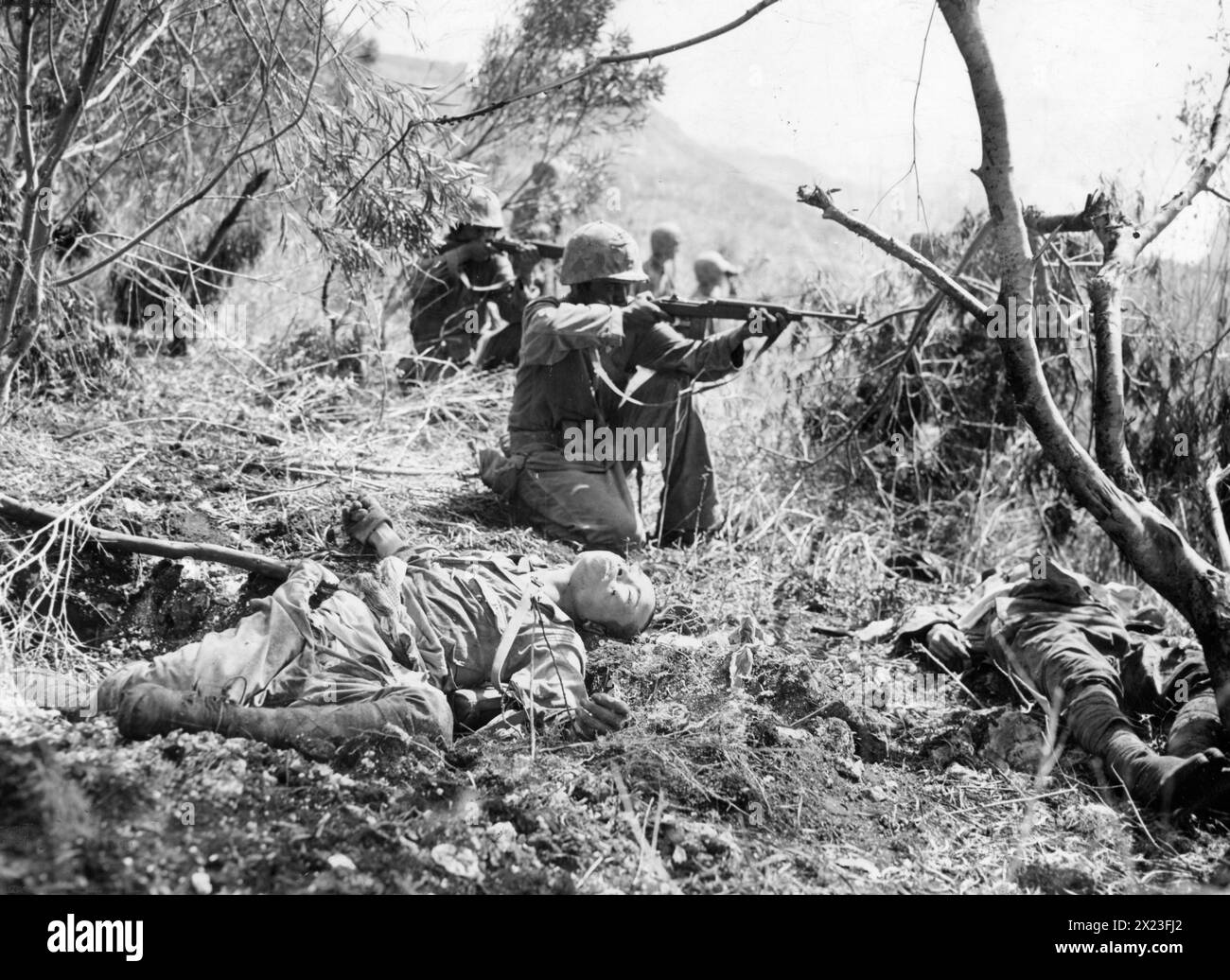 July 24, 1944, Saipan - U.S. Marines on Saipan fire at the enemy beside the bodies of Japanese dead as the Marines advance toward the western beach of the island near Mount Merpi.  By July 9, one day after Japanese resistance ended, Americans had buried more than 11,000 Japanese dead. Stock Photo