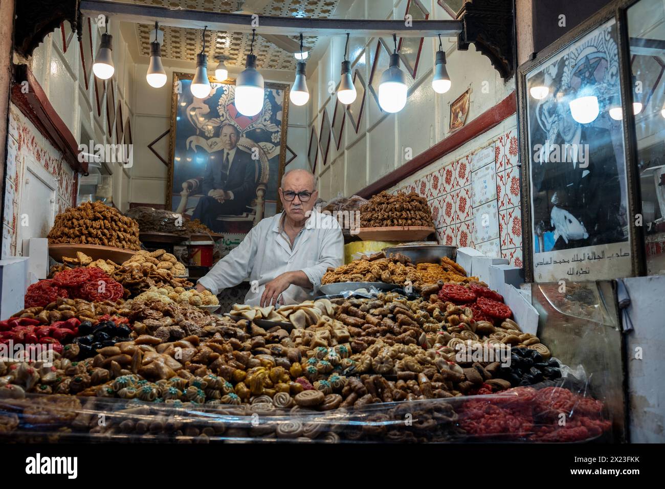 A Moroccan stall vendor selling varieties of dried fruits and nuts beneath the portraits of the former King Hassan II and current King Mohamed VI. Stock Photo