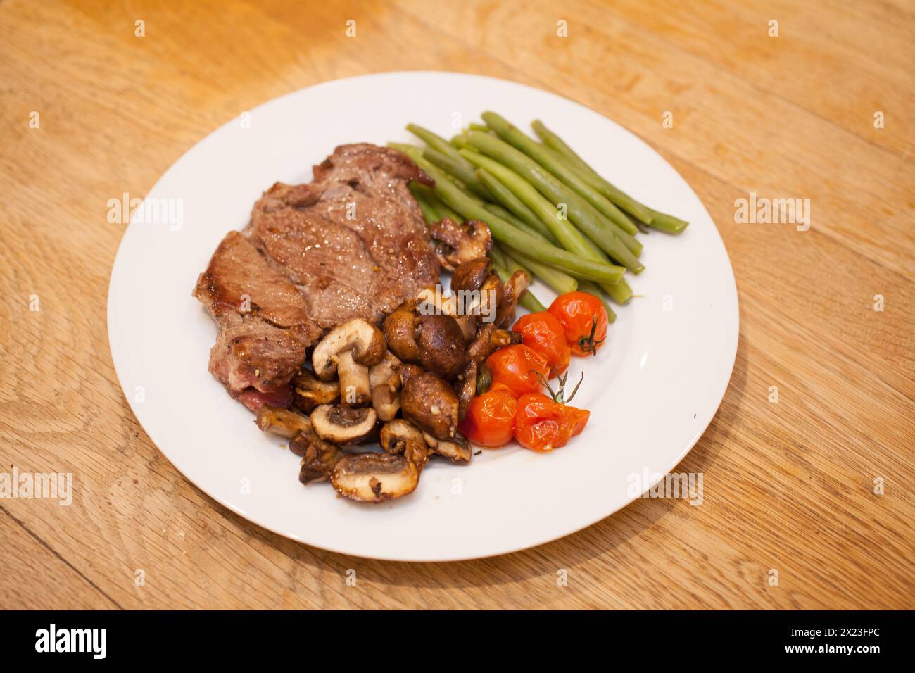 A cooked rib eye steak served with mushrooms, tomatoes and green beans ...