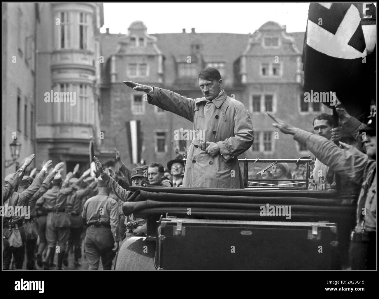 1930s Adolf Hitler in civilian clothing standing in the back of his open top Mercedes car, with a stern expression, giving a Heil Hitler salute to the passing Sturmbleitung paramilitary army marching past. Rudolf Hess featured under the Swastika flag. Hermann Goering also present standing in front of the Mercedes car. Standing next to Goering is Julius Streicher a notorious anti semite who started the Der Sturmer Newspaper to disseminate anti semitic  Nazi propaganda. Nurnberg Nuremberg Rally Nazi Gemany 1930s Stock Photo