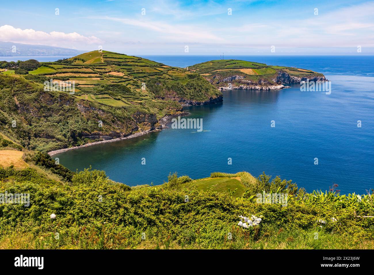 Lava rocks and agricultural fields stretch far out into the azure sea on a peninsula to the east of the Portuguese island of Flores, Azores, Portugal. Stock Photo