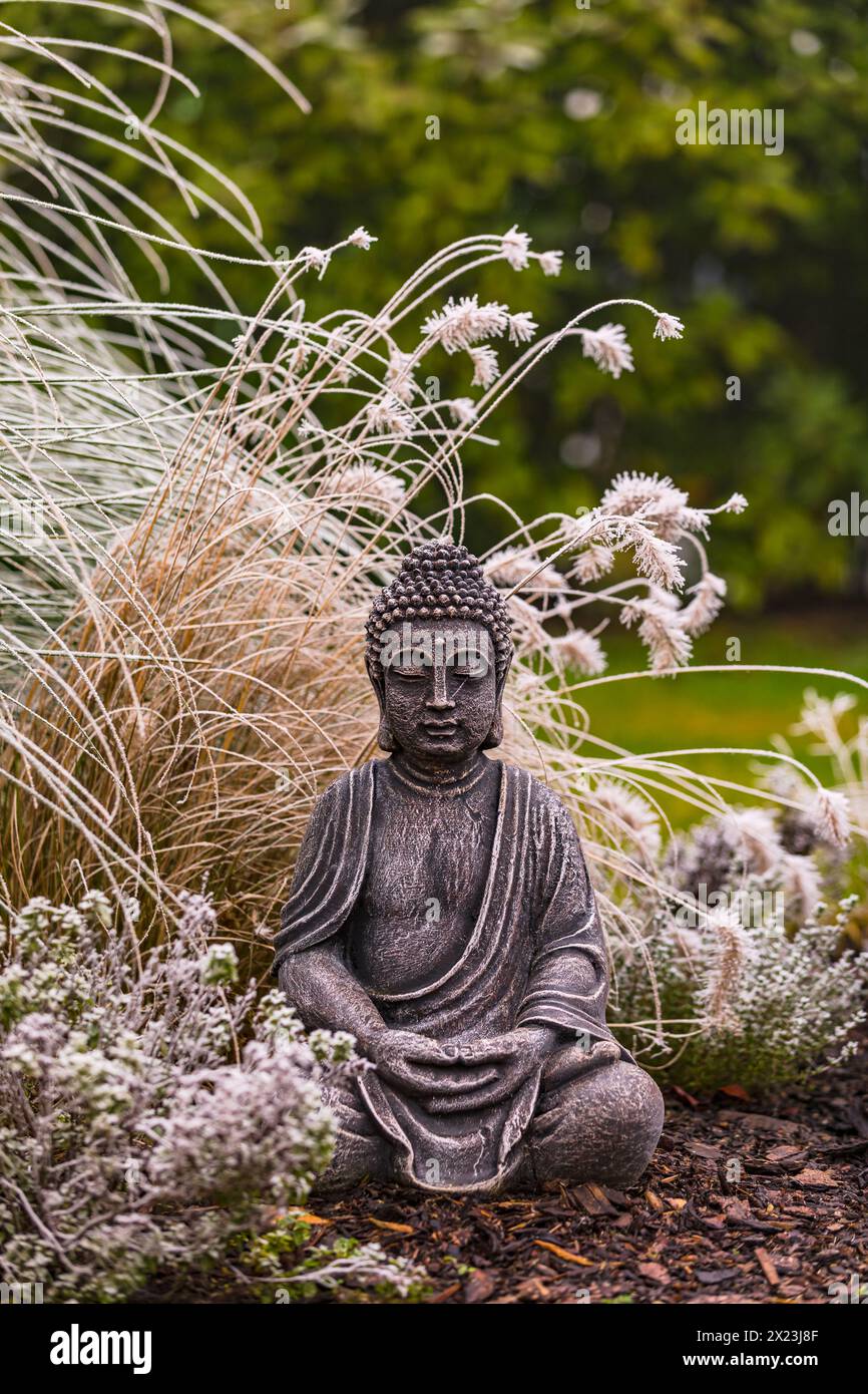 Sitting Buddha figure made of stone in the grass garden exposed in snow and ice Stock Photo