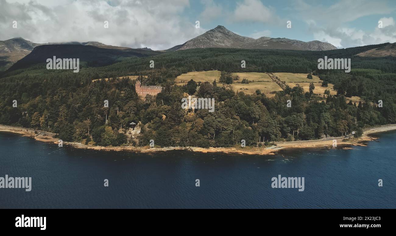 Scotland, Brodick ocean bay aerial view: alone sailboat at Firth-of-Clyde Gulf water against Scottish nature landscape. Beautiful mountains at horizon with wide woods. Panorama scenery shot Stock Photo