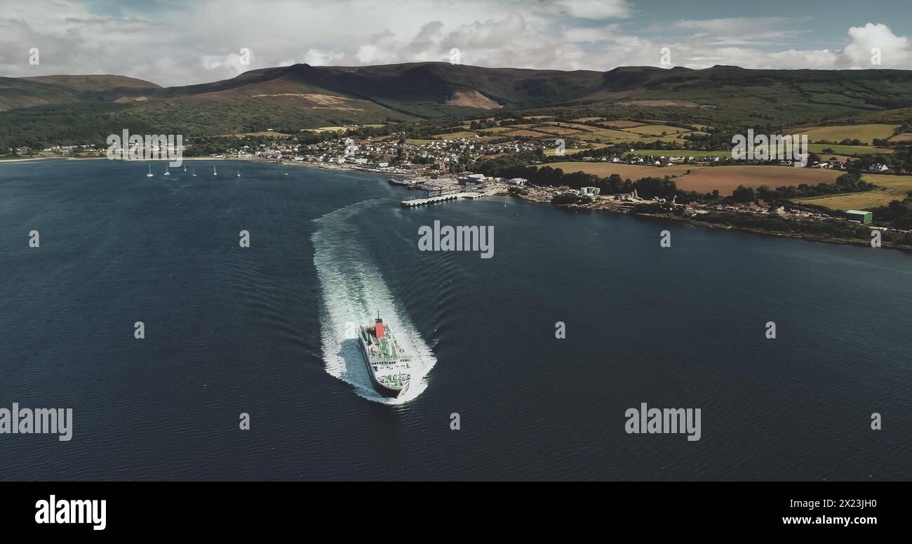 Scotland's ocean, passenger ferry aerial view in coastal water of Firth-of-Clyde Gulf. Ship crossing from Brodick terminal to Scottish mainland. Cityscape at green valleys. Stock Photo