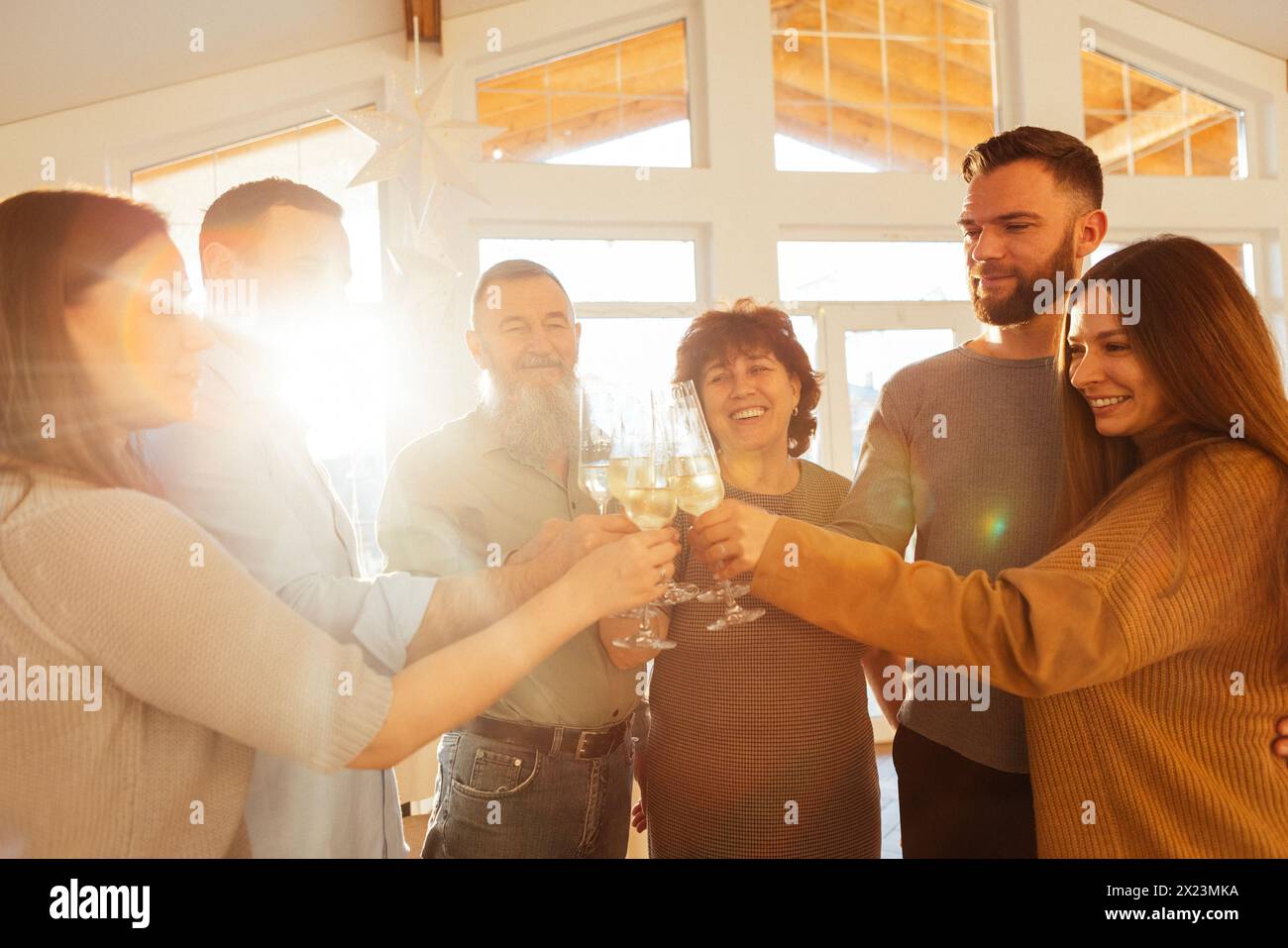 A mature married couple and their adult children raise glasses of champagne at home. Happy people of all ages make toast with sparkling wine in the li Stock Photo