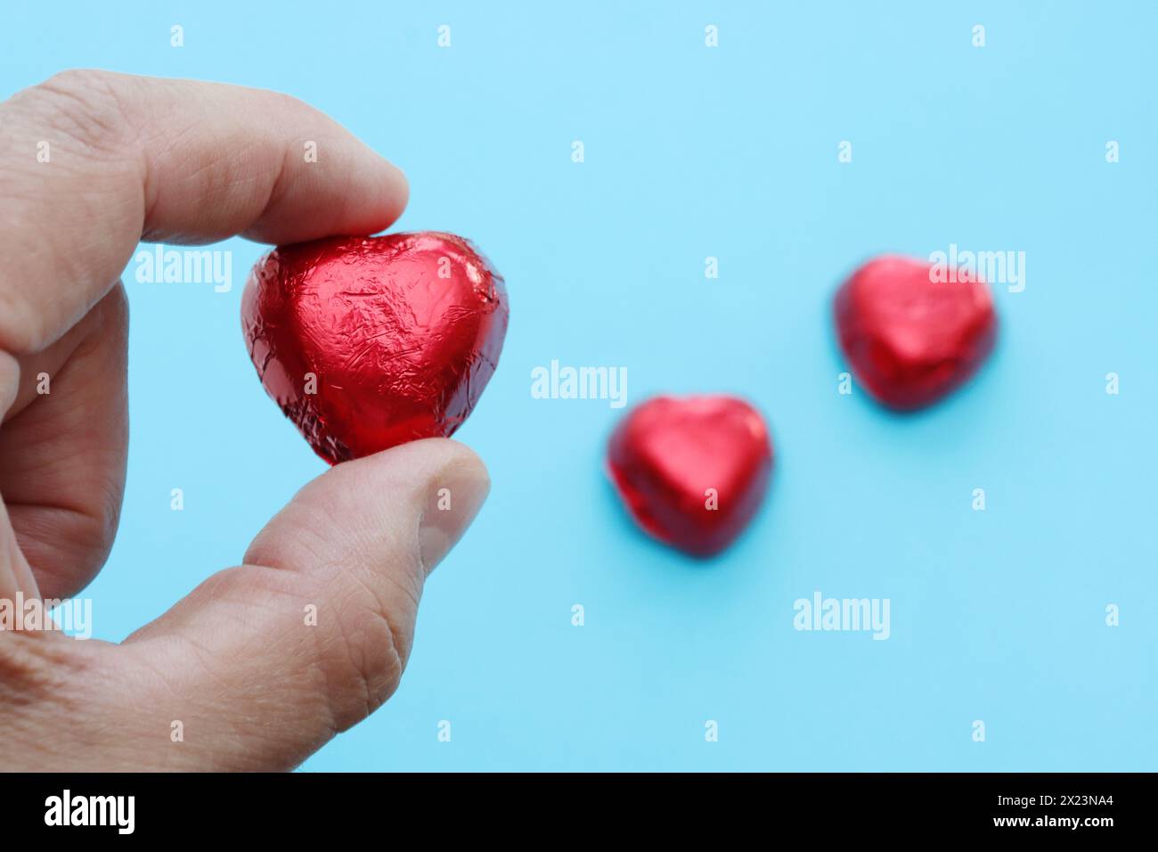 A close-up of a man's holds a red candy in the shape of a heart on a blue background. Stock Photo
