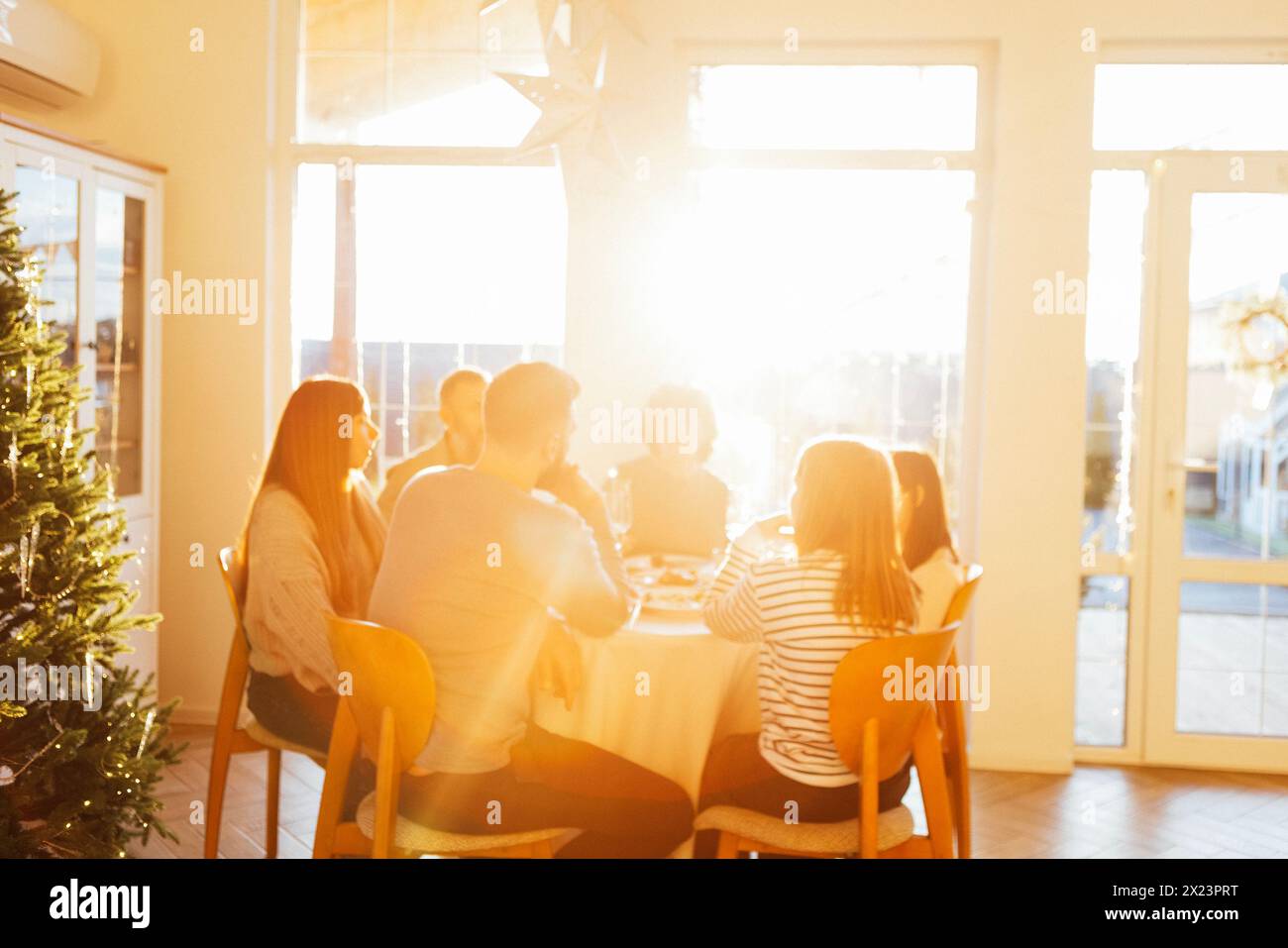 Happy big family at festive round table in rays of setting sun. Grandma, grandpa, mother, father and teenage daughters are having dinner in dining roo Stock Photo