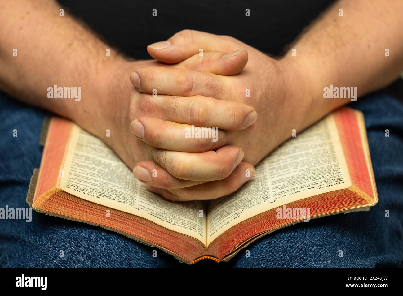 A man's praying hands on an open Bible. Stock Photo