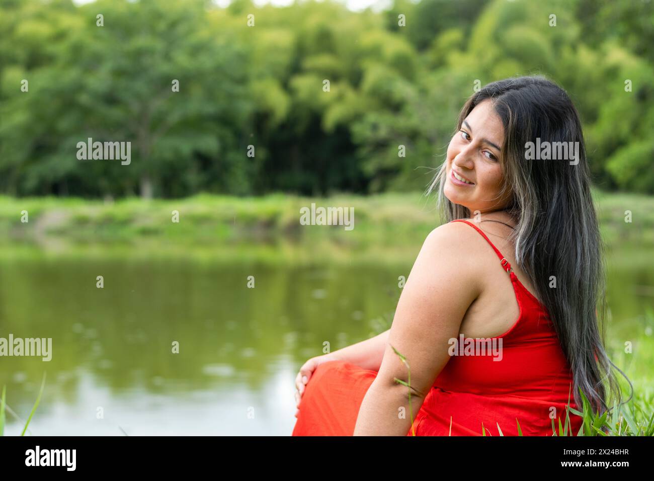 latina woman sitting by a lake looking back, with a big smile on her face  Stock Photo - Alamy