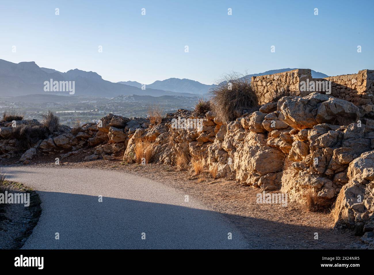 A walking path, trail, meanders past ancient stone walls with a backdrop of majestic mountains bathed in the golden hour light. High quality photo Stock Photo