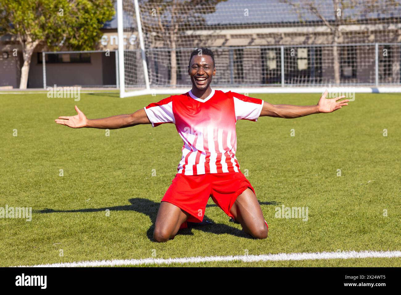 African American young male athlete kneeling on soccer field outdoors, arms wide open Stock Photo