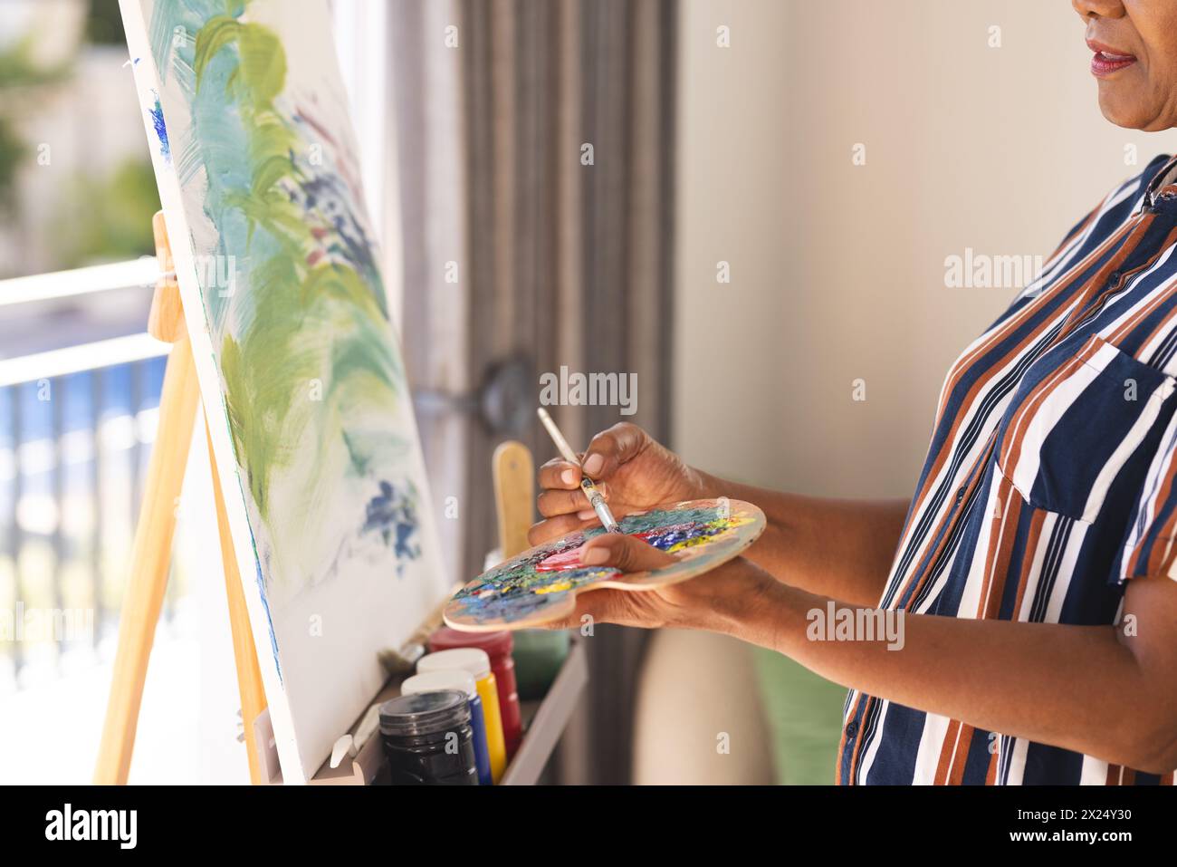 African American senior woman painting on canvas at home, holding palette Stock Photo