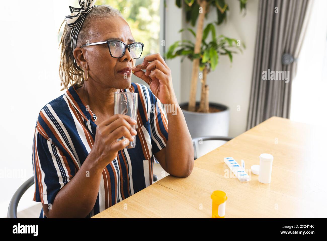 African American senior woman at home holding glass of water, taking medicine Stock Photo