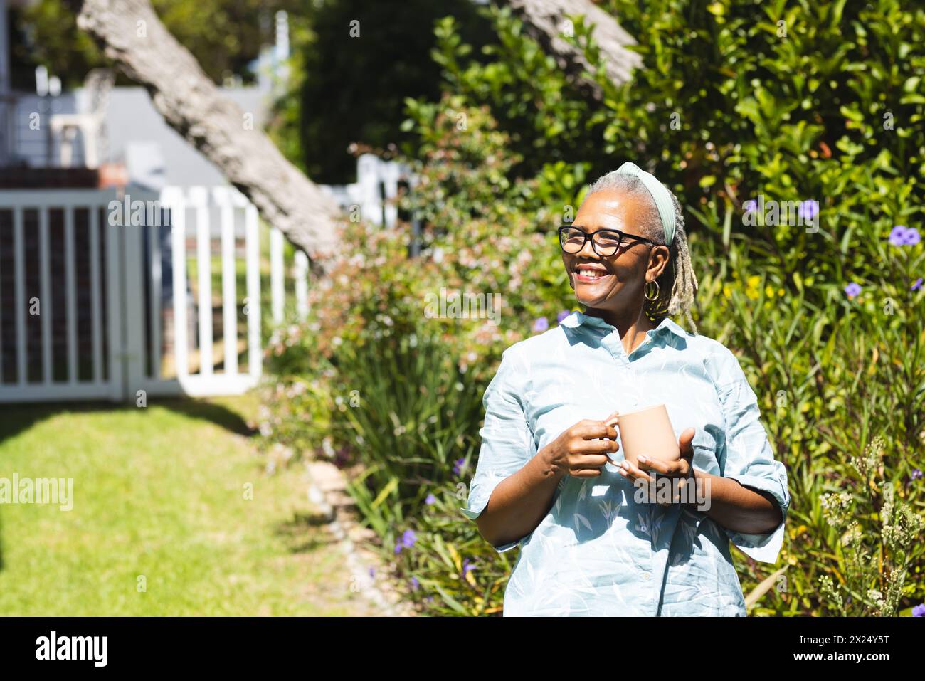 African American senior woman holding book, standing in sunny garden at ...