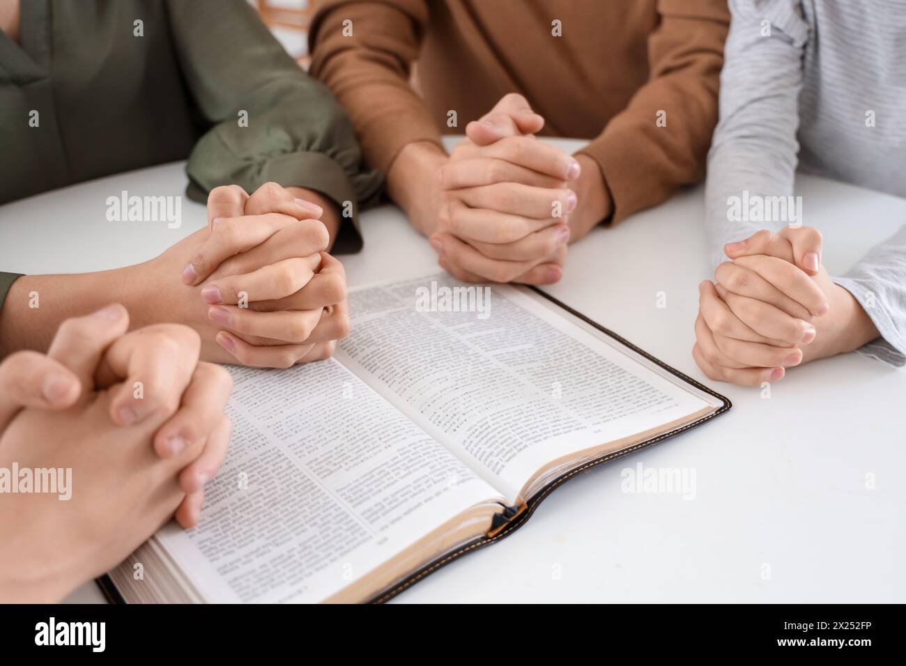 Family praying with Holy Bible on table in kitchen, closeup Stock Photo
