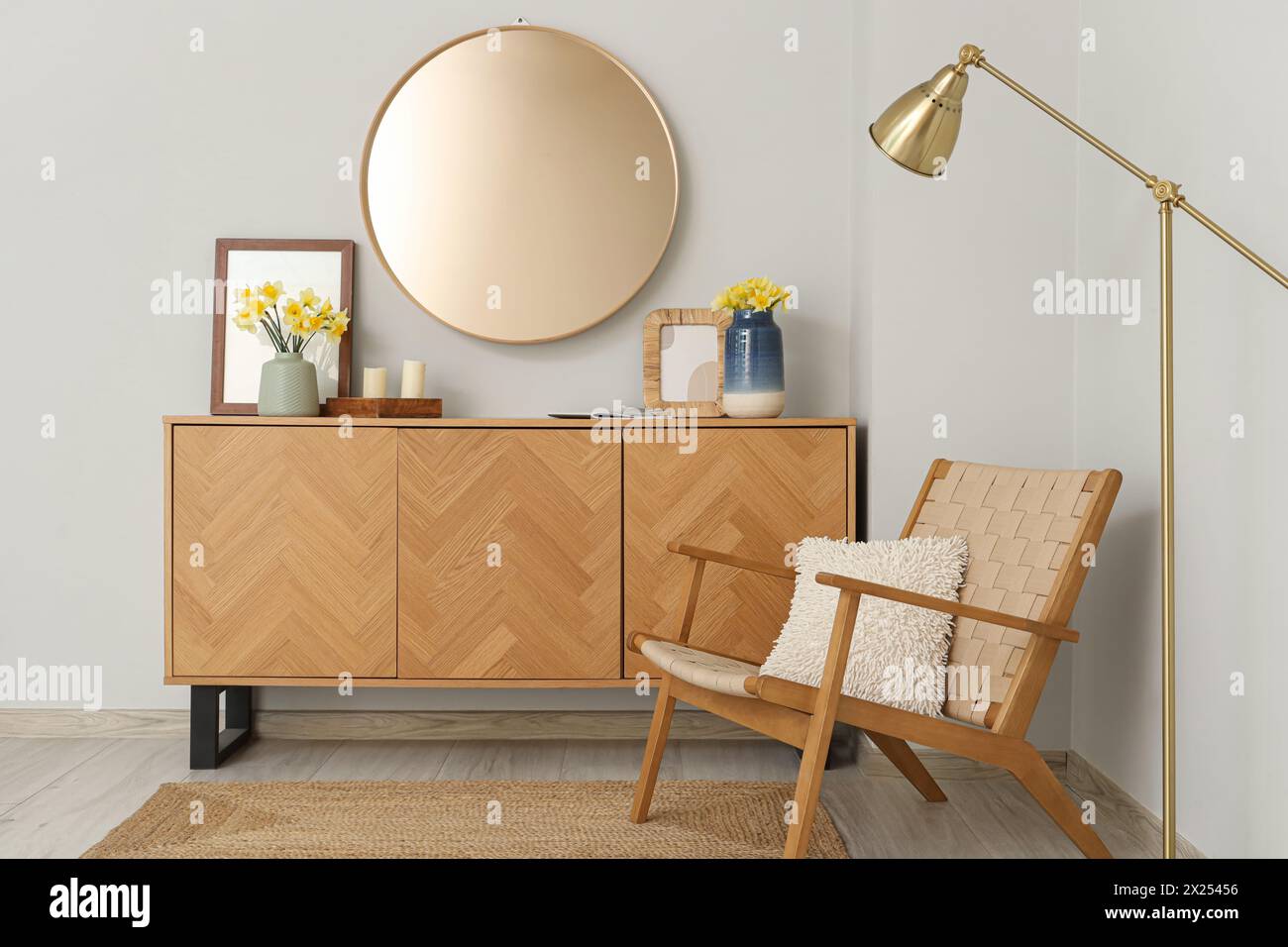 Chest of drawers, armchair and vase with narcissus flowers in living room Stock Photo