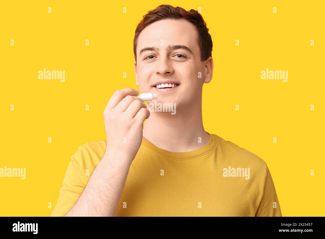 Handsome young man applying lip balm on yellow background Stock Photo