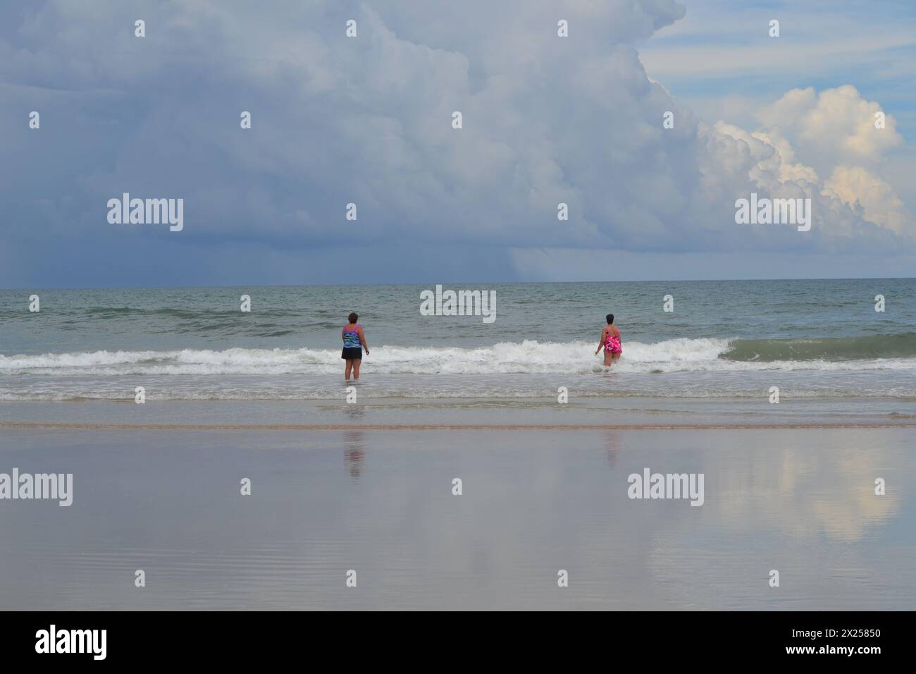 Two women stand at the water's edge as a foreboding rainstorm approaches Daytona Beach, Florida. Stock Photo