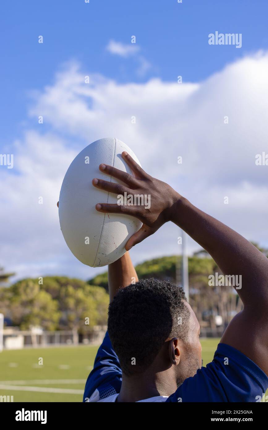 African American young male athlete holding a rugby ball, ready to throw, on field outdoors Stock Photo