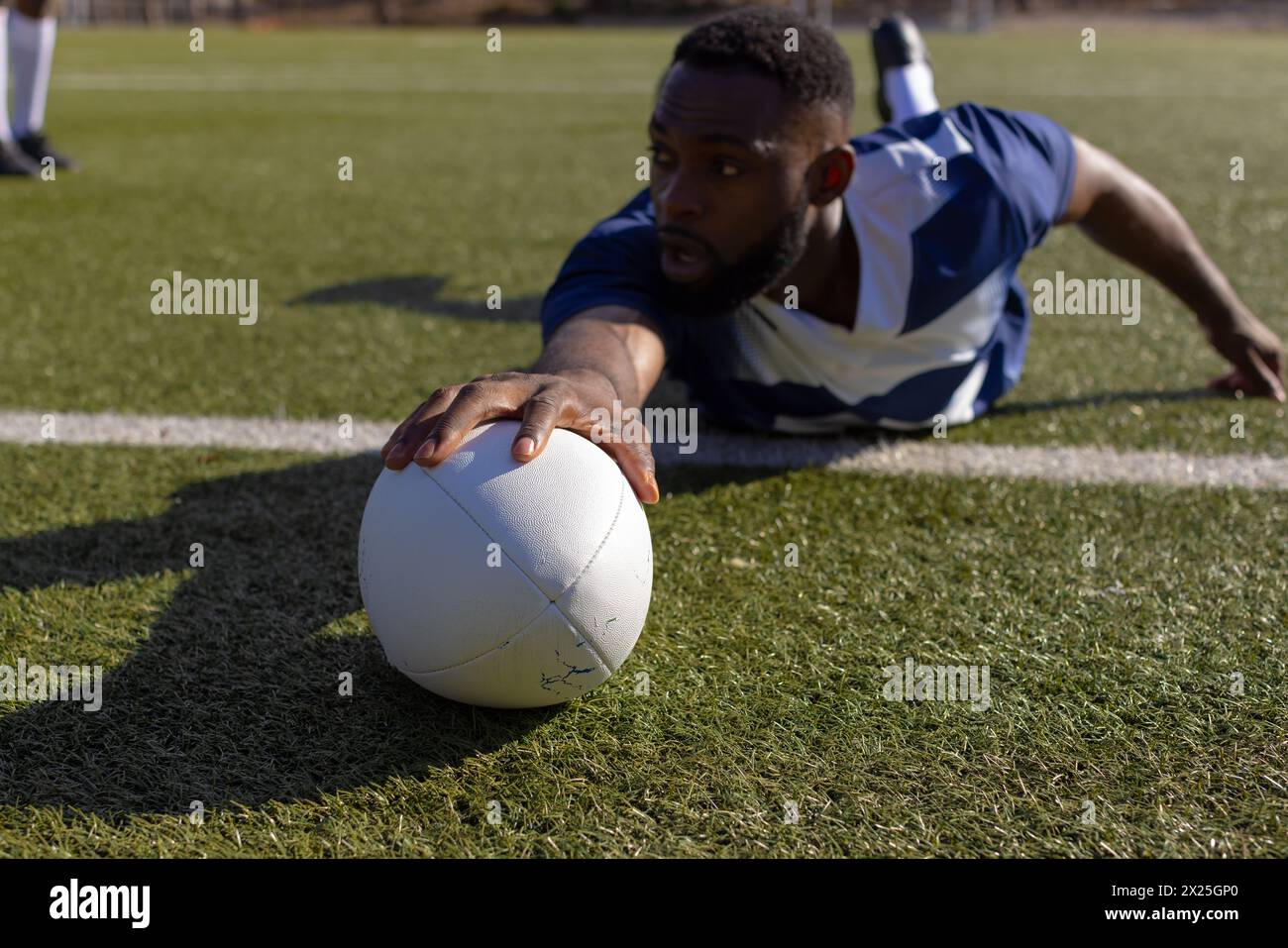 African American young male athlete reaching for a rugby ball on grass to score a try Stock Photo