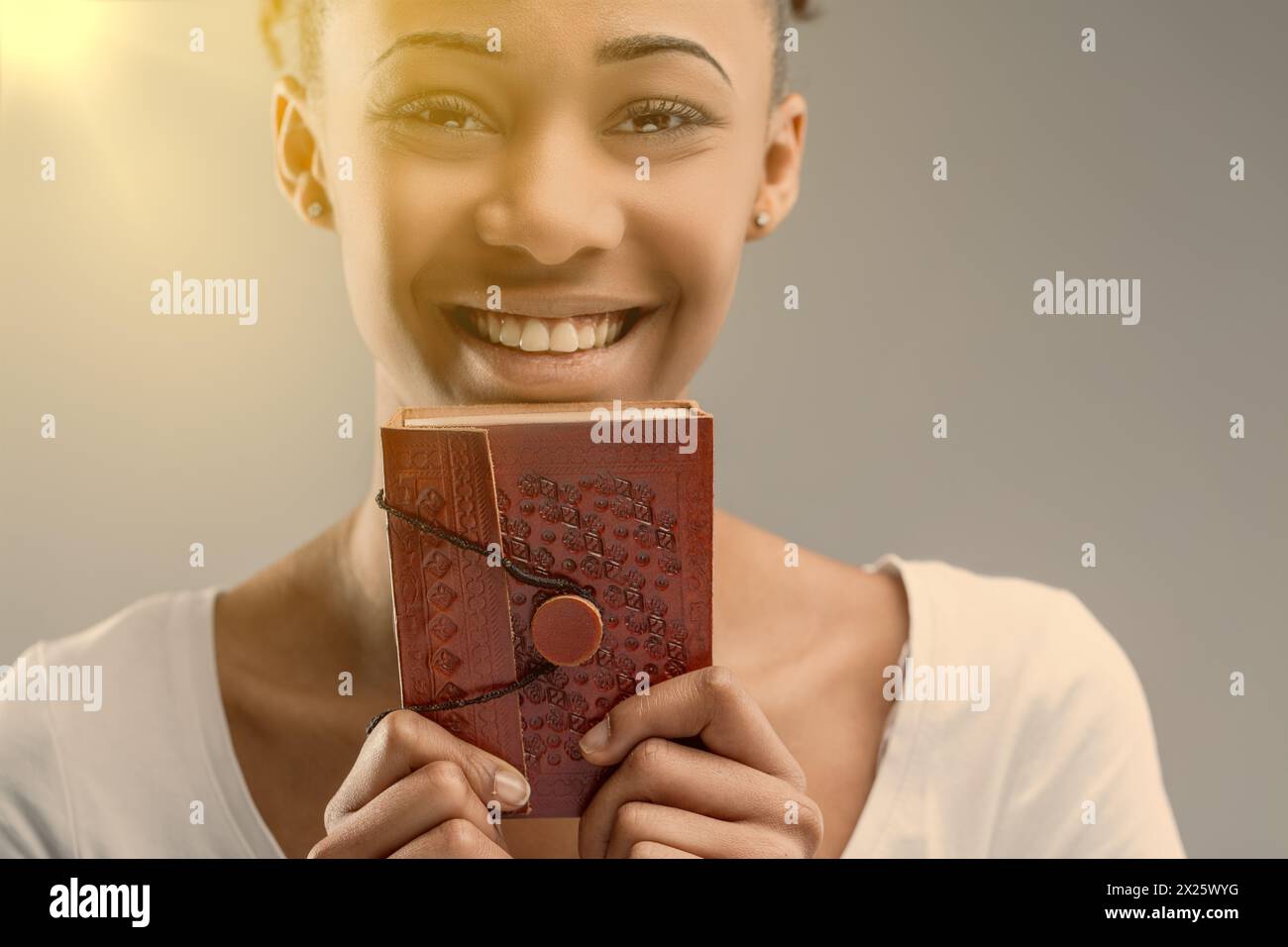 Glimpse into the soulful eyes of a young woman behind a red, embossed leather journal Stock Photo