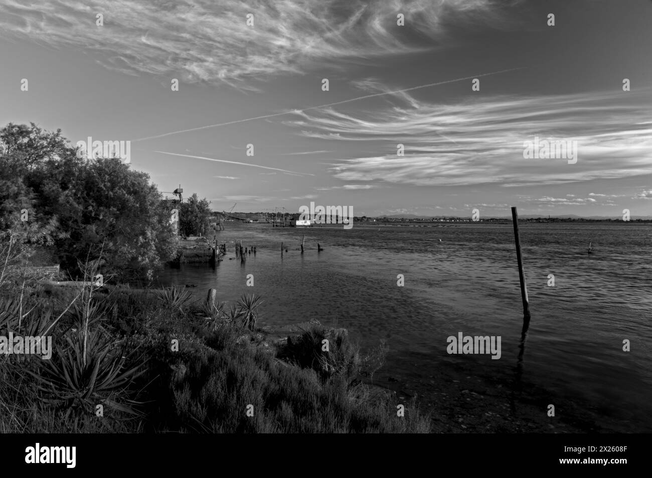 Tranquil waters embrace a picturesque scene of fishing boats and rustic huts along the shores of Pialassa dei Piomboni, near Ravenna Stock Photo