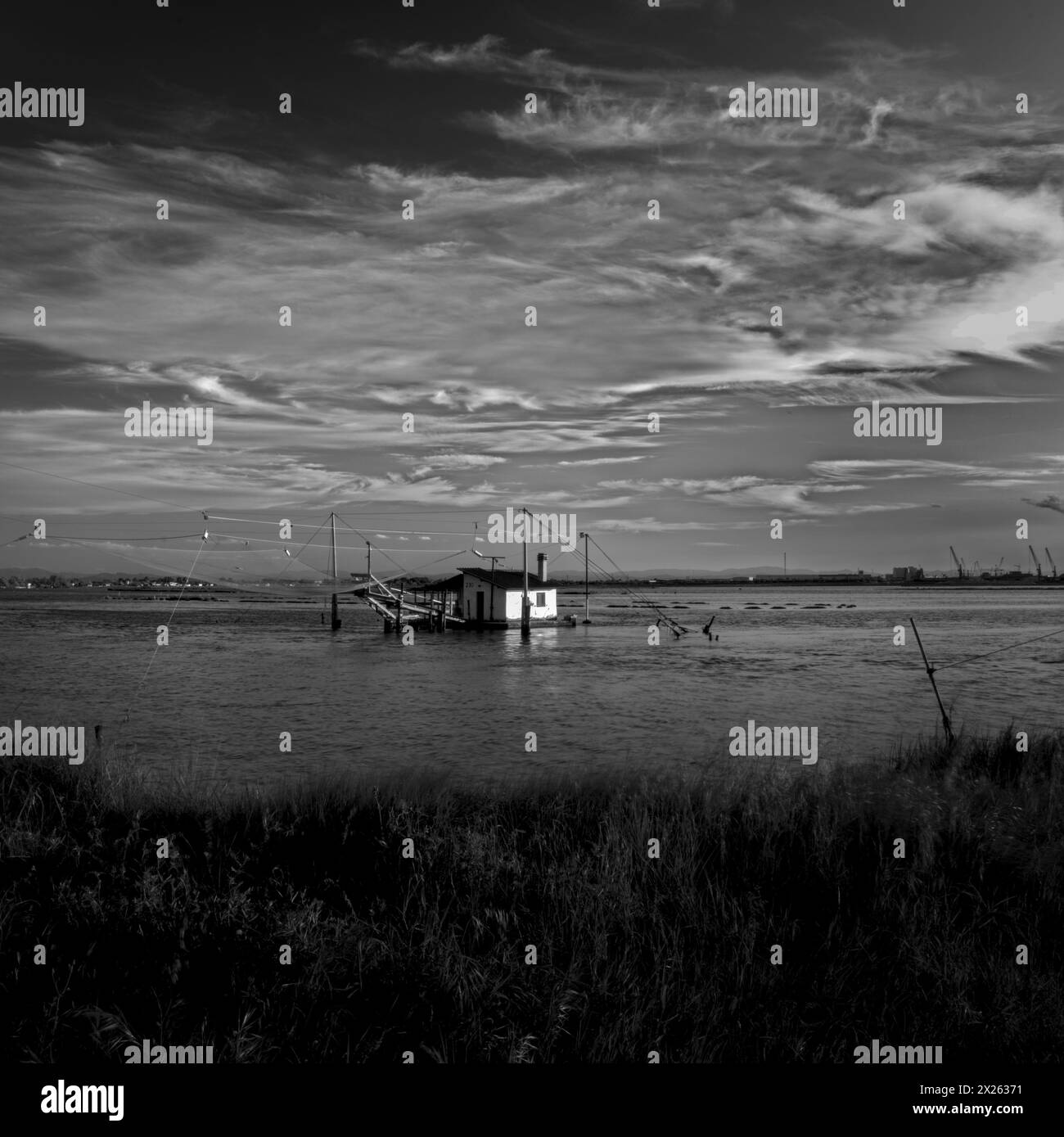 Tranquil waters embrace a picturesque scene of fishing boats and rustic huts along the shores of Pialassa dei Piomboni, near Ravenna Stock Photo