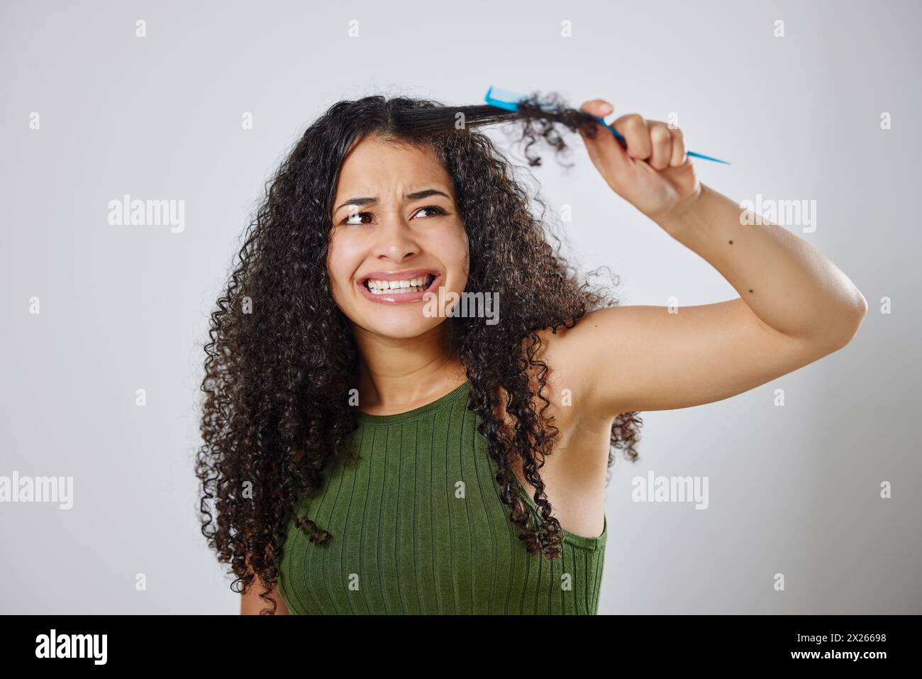 Messy hair, knot and scared woman with comb in studio for tangle, stress and problem on grey background. Curly, haircare and model with anxiety for Stock Photo
