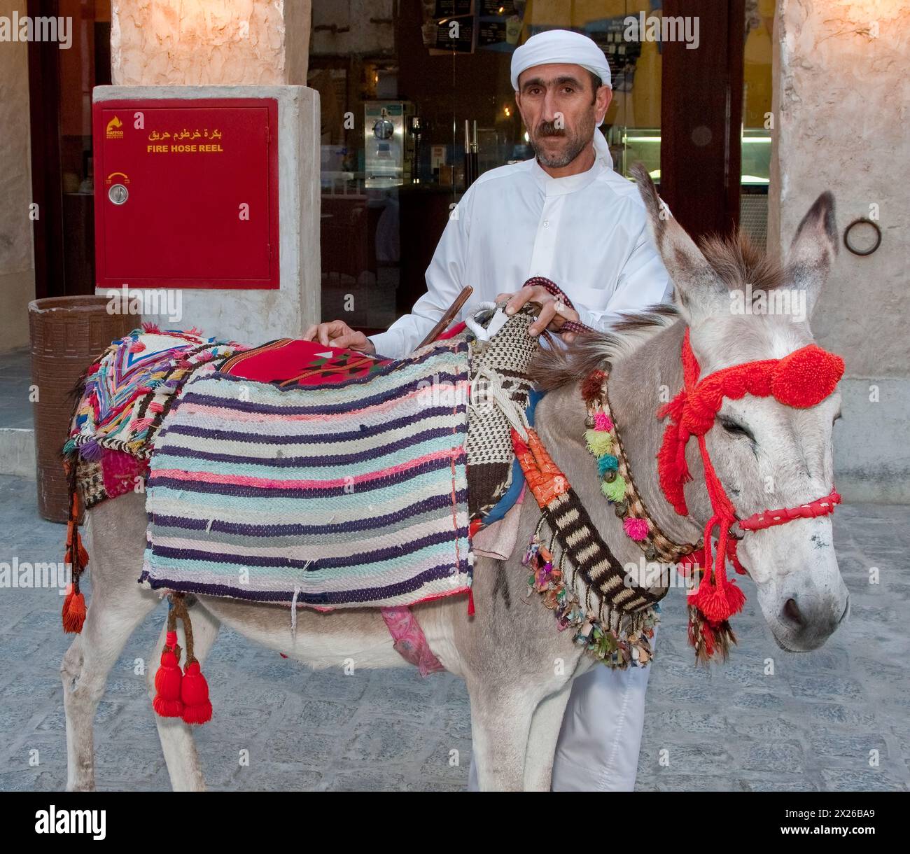 Doha, Qatar.  Qatari Man Wearing a Traditional Dishdasha Offers Rides on a Donkey to Qatari Children in the Market. Stock Photo