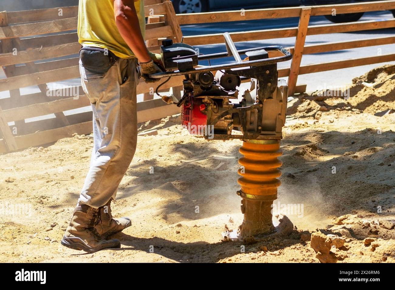 Construction worker compacting soil in house foundation using compactor. Work with tamping