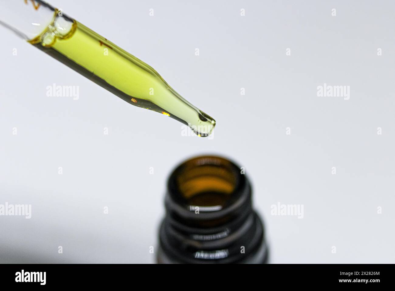 Close up of a glass pipette dropper filled with CBD oil over a small brown glass bottle on white background Stock Photo