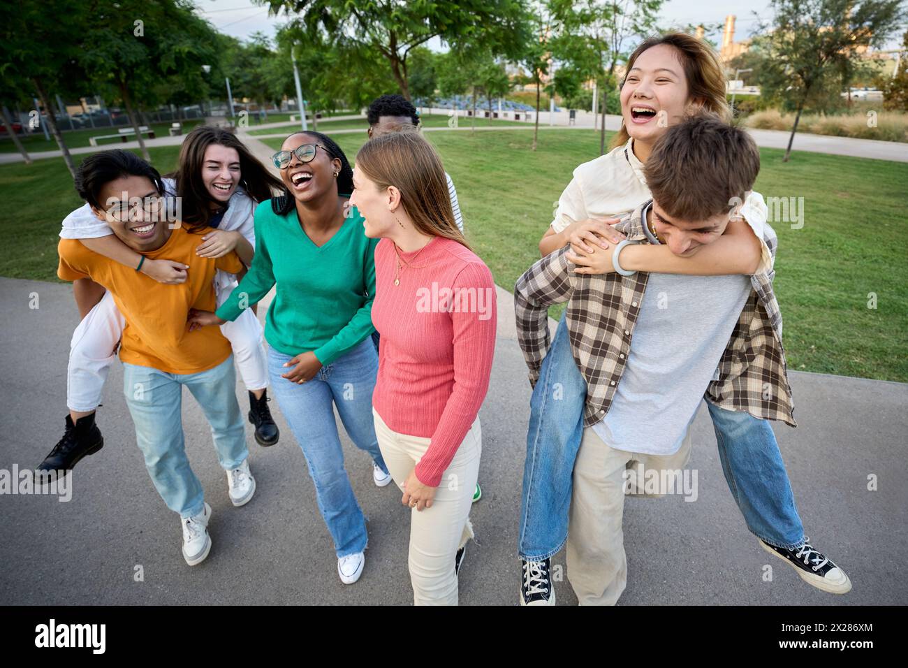A large multiracial group of teenagers laughing and having fun piggybacking together Stock Photo