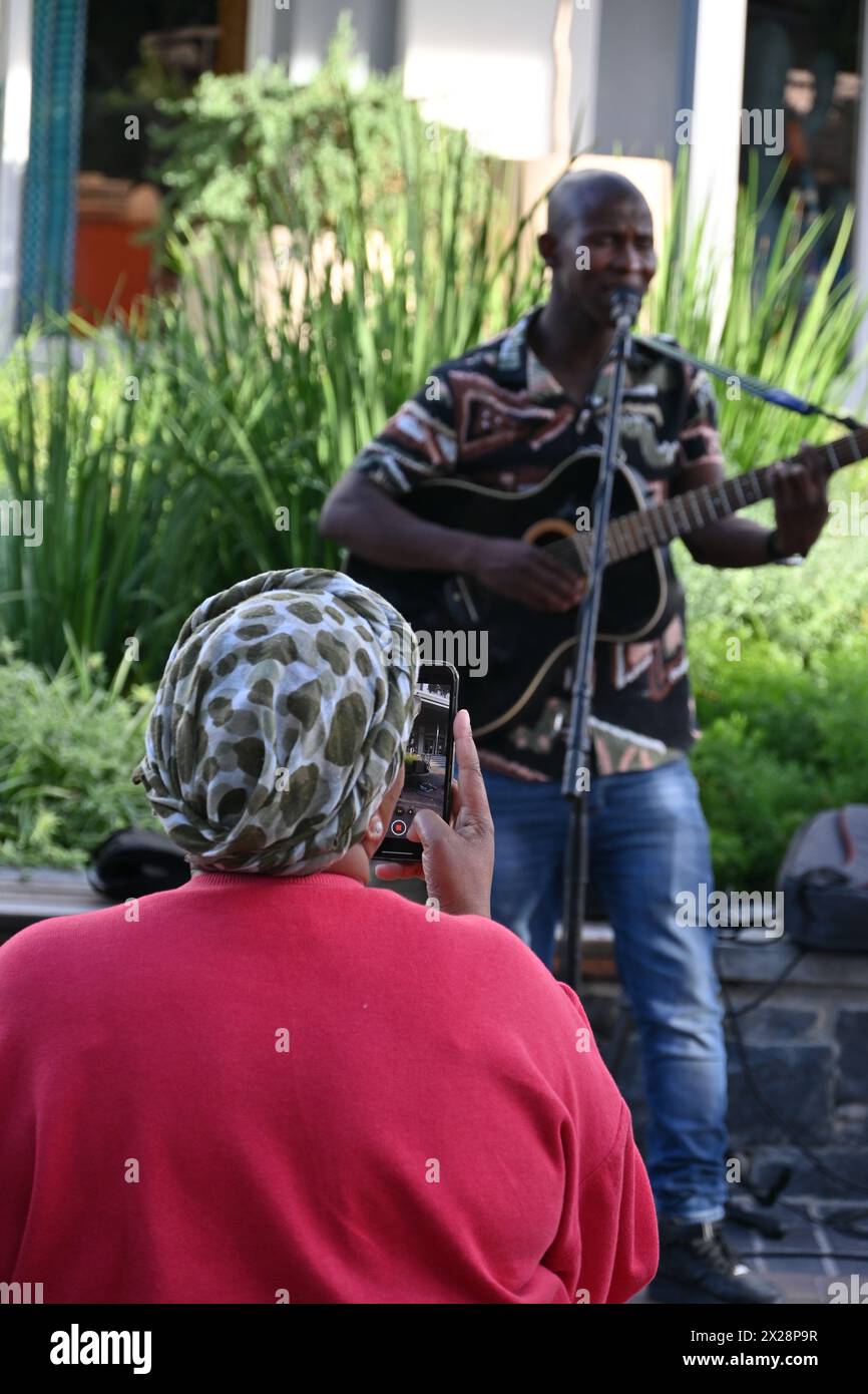 Black woman taking photo of a guitarist playing on the street in