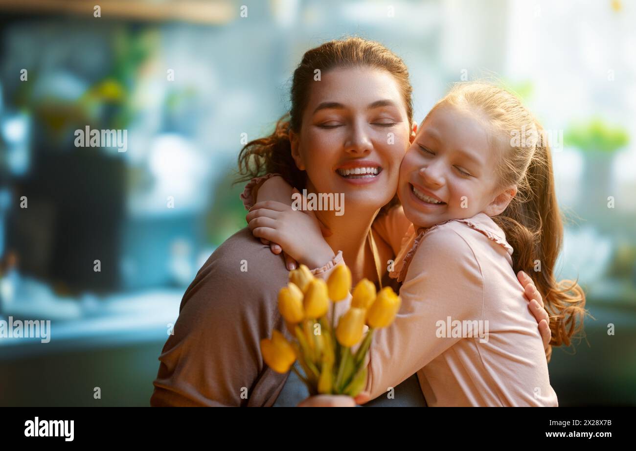 Happy mother's day. Child daughter is congratulating mom and giving her flowers. Mum and girl smiling and hugging. Family holiday and togetherness. Stock Photo