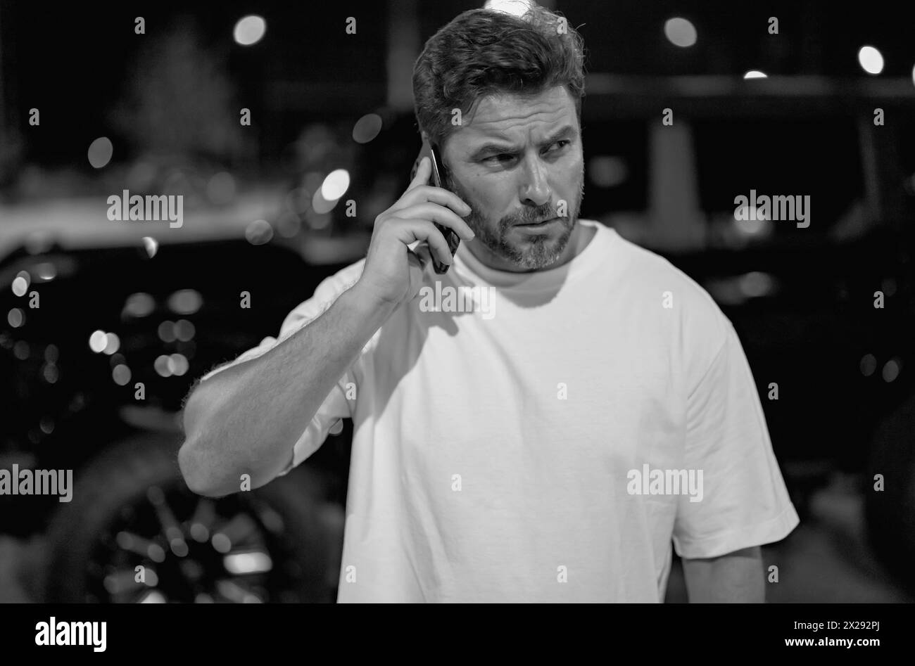 Angry man talking on phone on night urban street. Dangerous aggressive man talking on phone with serious face. Criminal city danger district Stock Photo