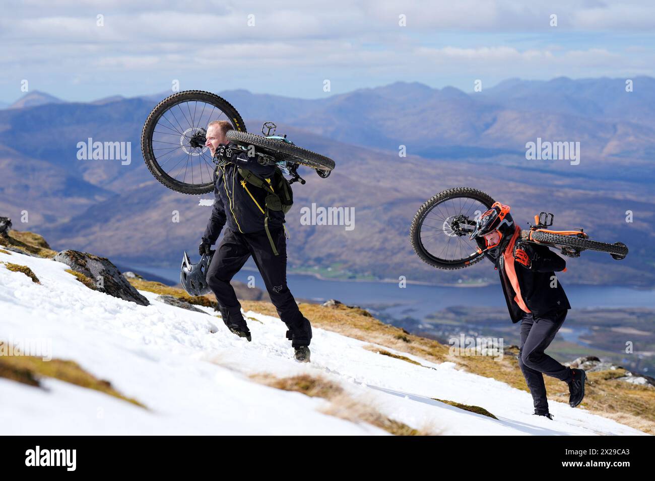 Cyclists climb with their bikes to the start-line to take part in MacAvalanche, a mass mountain bike race through the snow, descending over 900m from the summit of Aonach Mor in the Nevis Range near Fort William. Picture date: Saturday April 20, 2024. Stock Photo