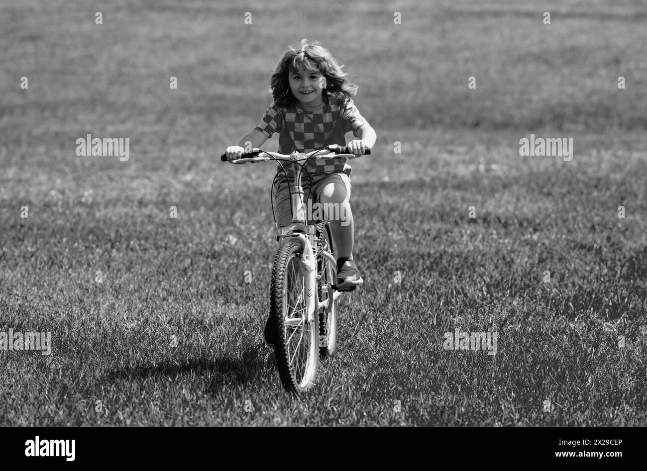 Little kid boy ride a bike in the park. Kid cycling on bicycle. Happy smiling child riding a bike. Boy start to ride a bicycle. Sporty kid bike riding Stock Photo