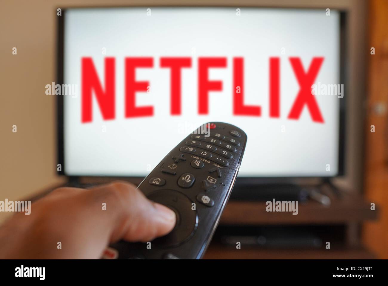 April 20, 2024, Brazil. In this photo illustration, a hand holding a TV remote control in front of the Netflix logo on a TV screen Stock Photo