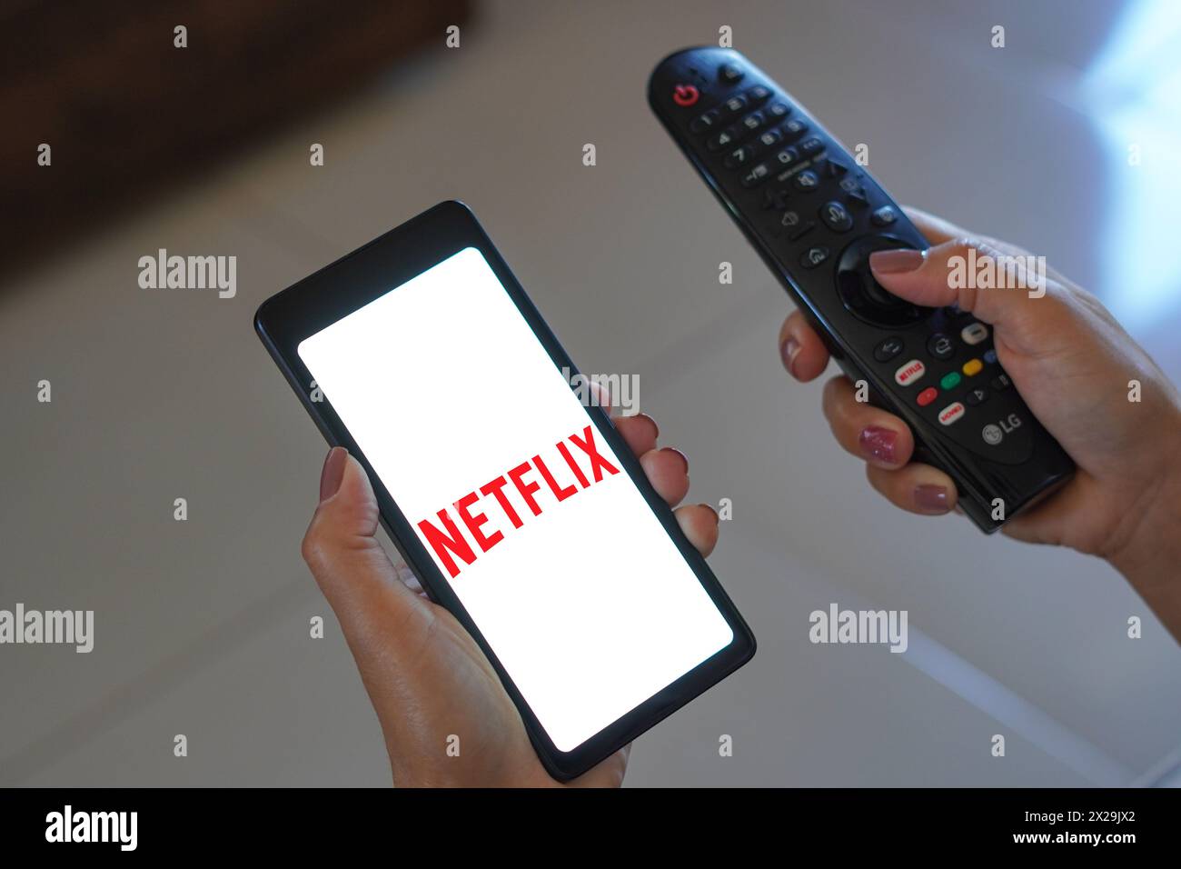 April 20, 2024, Brazil. In this photo illustration, the woman holds the TV remote control and the smartphone with the Netflix logo displayed on the sc Stock Photo