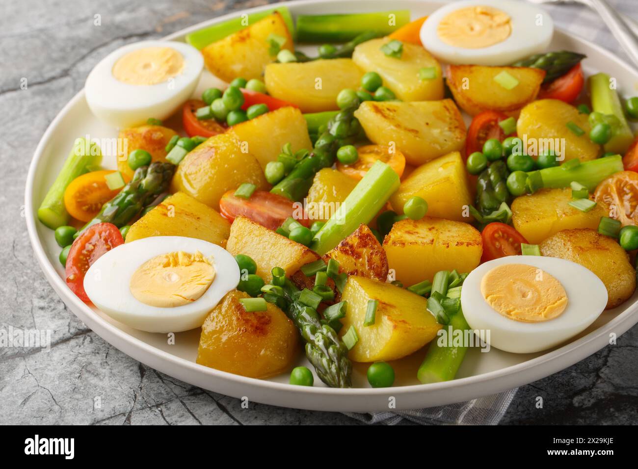 Salad with roasted potatoes, asparagus, boiled egg, tomato and peas closeup on the plate on the table. Horizontal Stock Photo