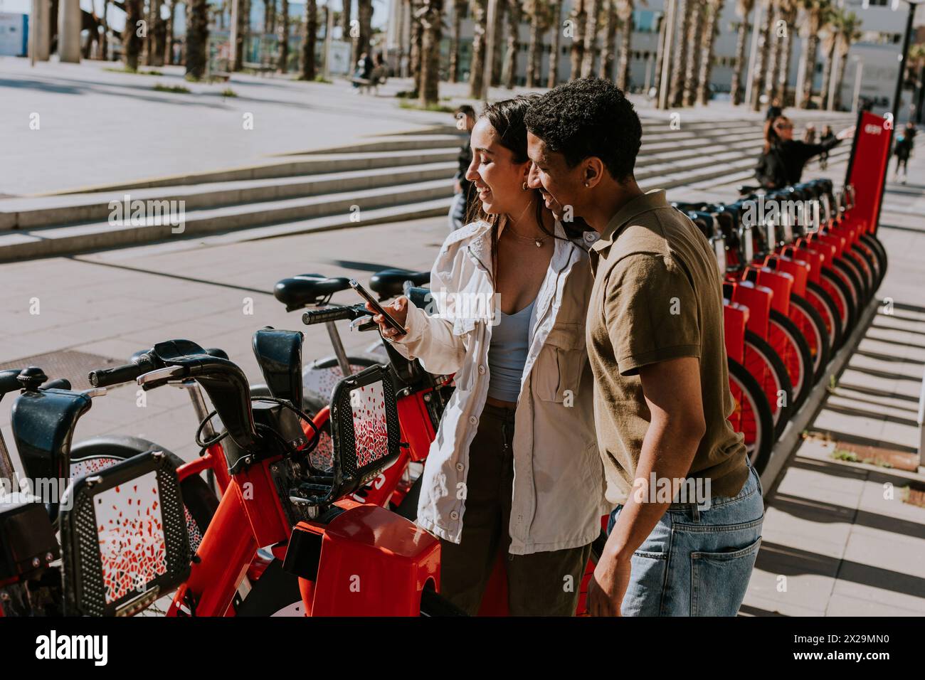 Young pair enjoying a breezy day choosing bikes from a rental station in Barcelona. Stock Photo