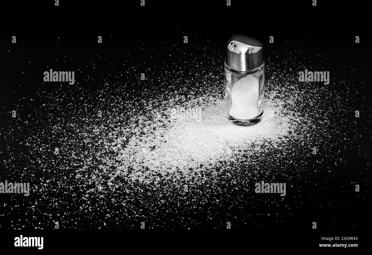 Scattered salt on a black background and a stem salt shaker. Close-up Stock Photo