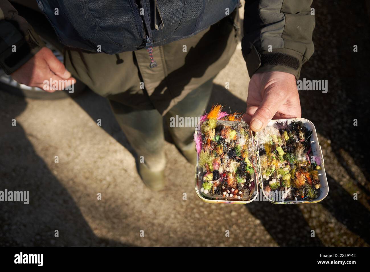 A fisherman, dressed in green, shows off his box of fishing flies. Stock Photo