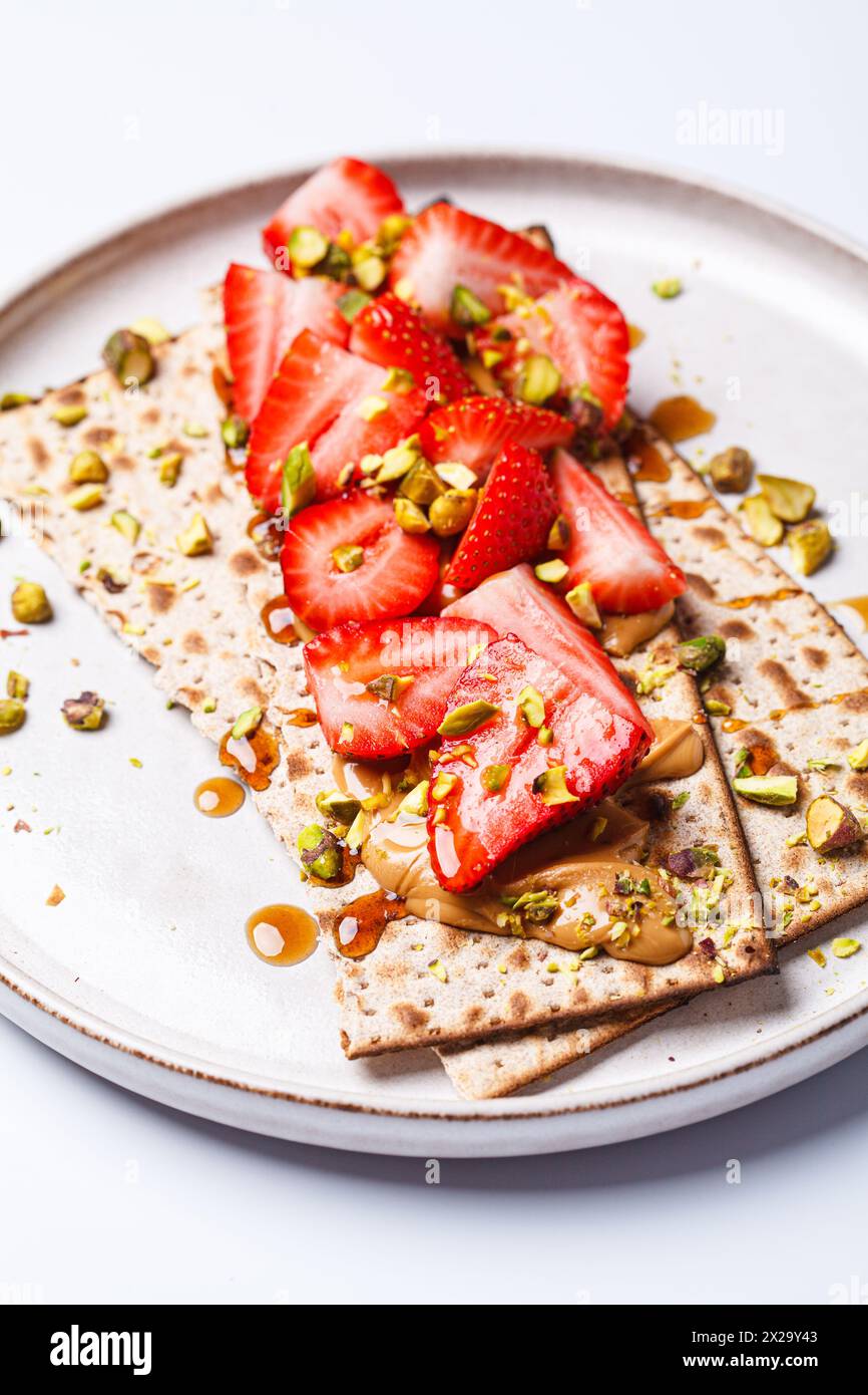 Matzo toast with peanut butter, strawberries and pistachios on a white