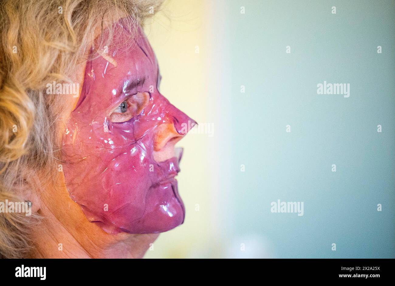 Mature middle aged woman using a purple gel face mask for skin and beauty care Stock Photo
